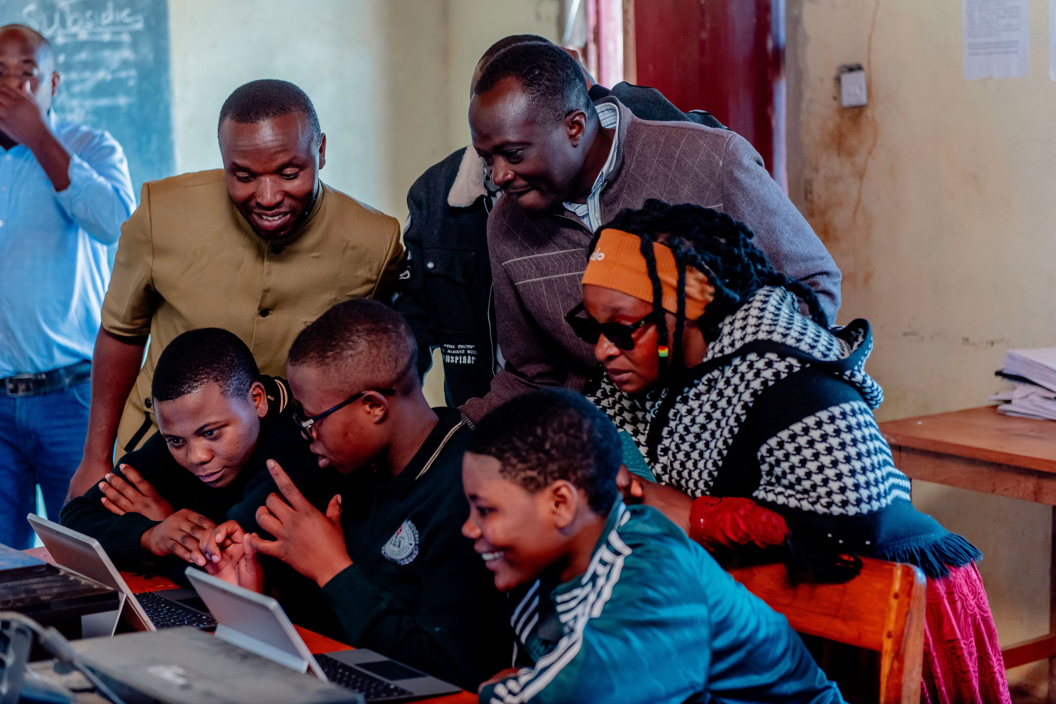 Students and adults gathered around a screen in a classroom