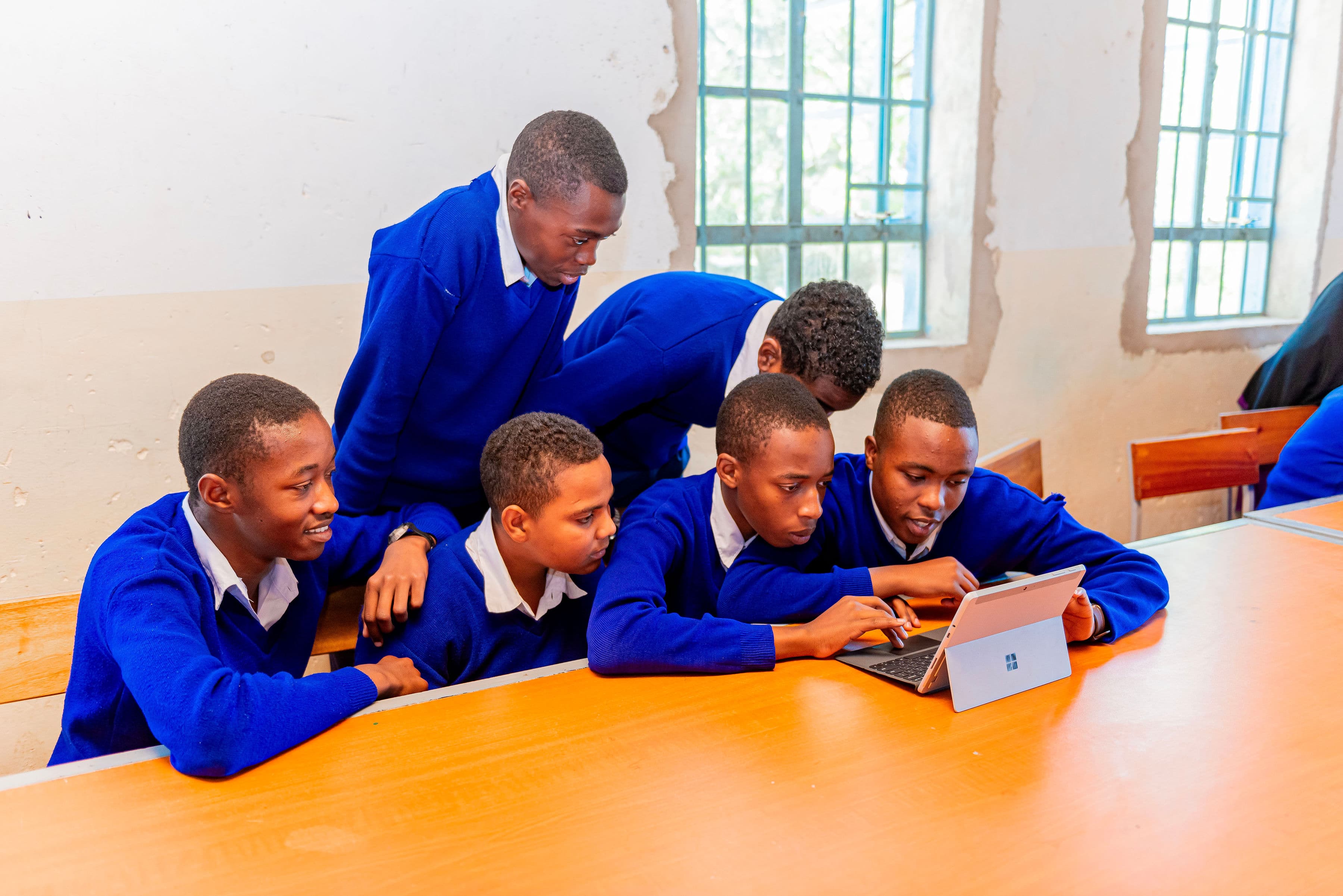 Students in blue uniforms looking at a tablet together