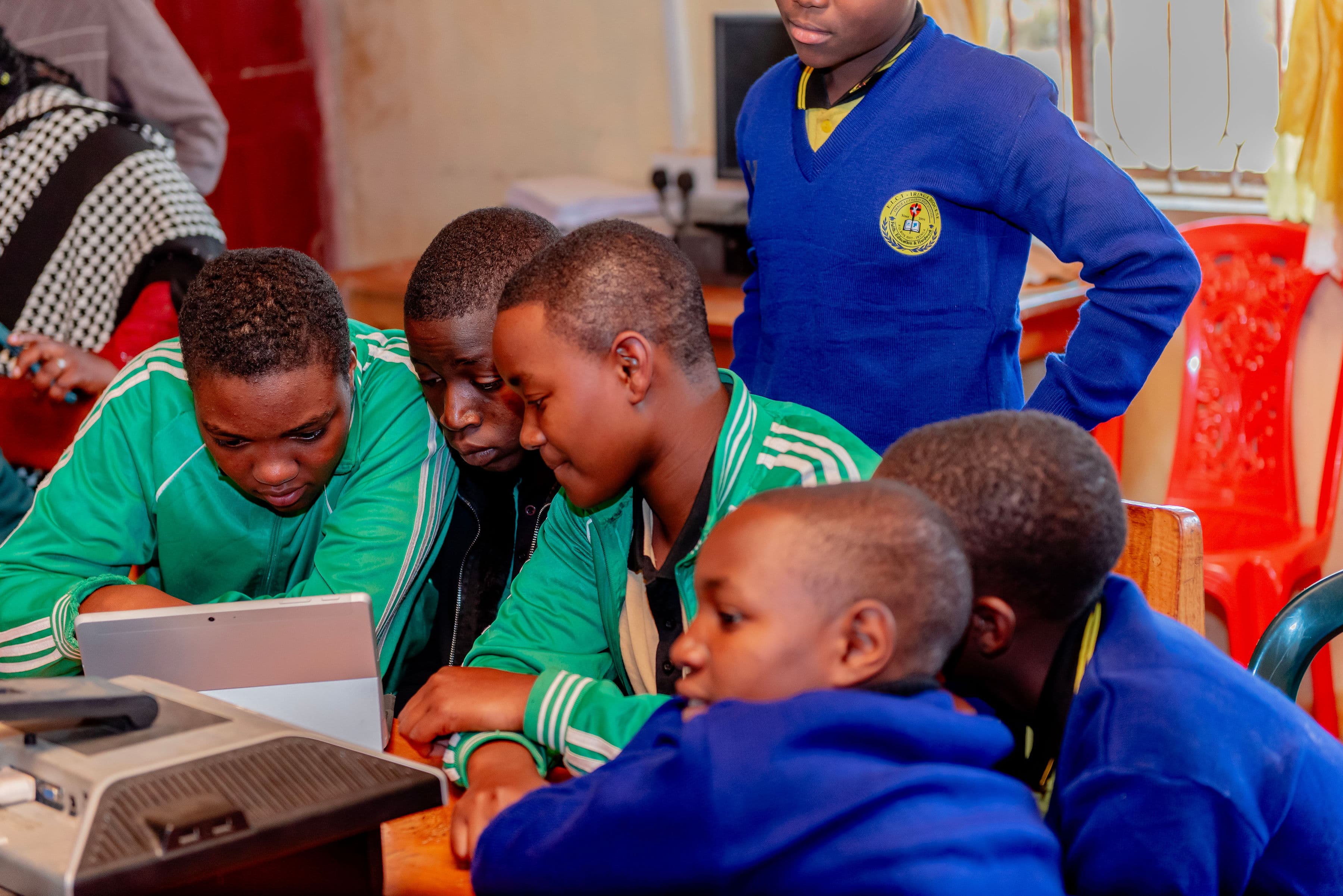 Students in green and blue uniforms gathered around a learning device