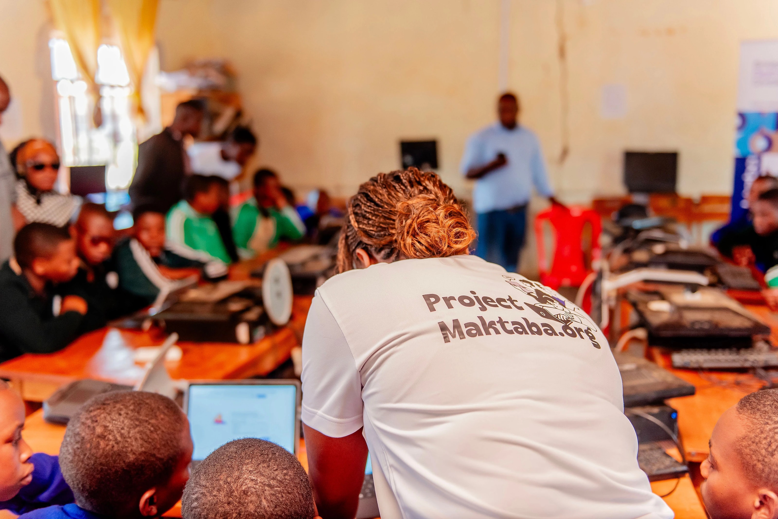 A Project Maktaba team member working through a lesson with students at their laptops